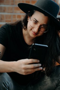 Cep telefonu kullanan, gözlüklü, siyah şapkalı bir kadının portresi..