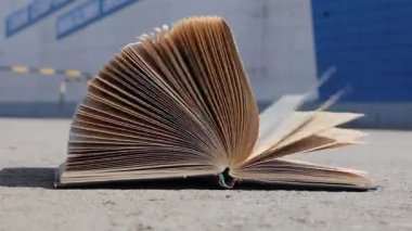 Kitabın sayfalarını rüzgârda çevir. Kitap asfaltta yatıyor..