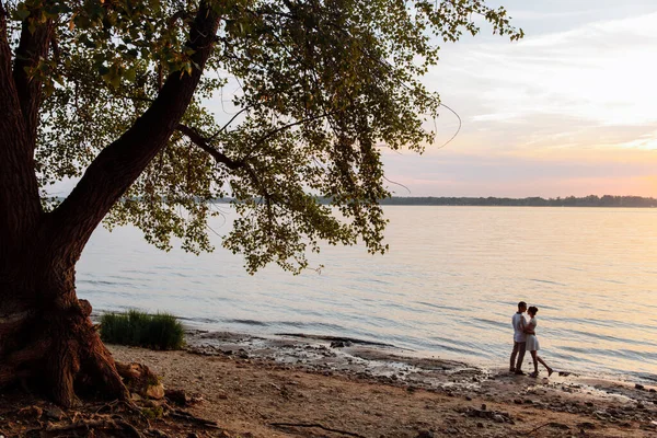 İki genç nehir kıyısında yaşlı bir ağacın altında sarılıyor.. 