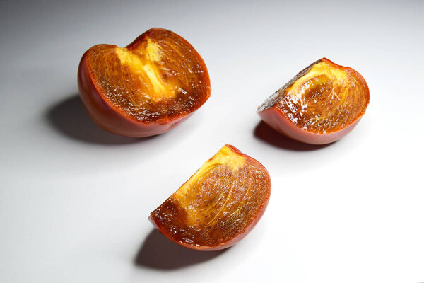 fresh ripe persimmons with slices, on a light background with hard light. One cut slice in foreground in focus, background soft focus.