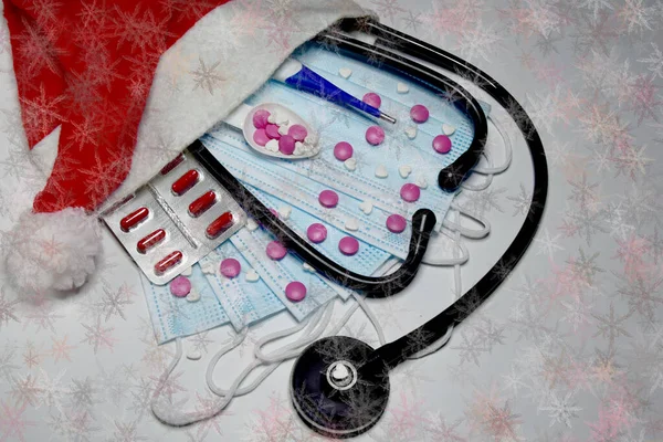 Tıbbi steteskop, tıbbi maskeler, haplar ve arka planda Noel Baba şapkası takan bir termometre. Noel ve Yeni Yıl konsepti. Yaratıcı tıbbi kış geçmişi, kartpostal.