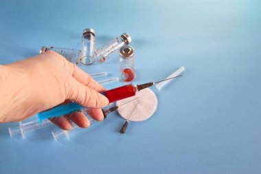 Cam şişelerin ve kullanılmış şırıngaların mavi arka planında elinde şırınga ve sığ bir alan derinliği olan bir şırınga var..