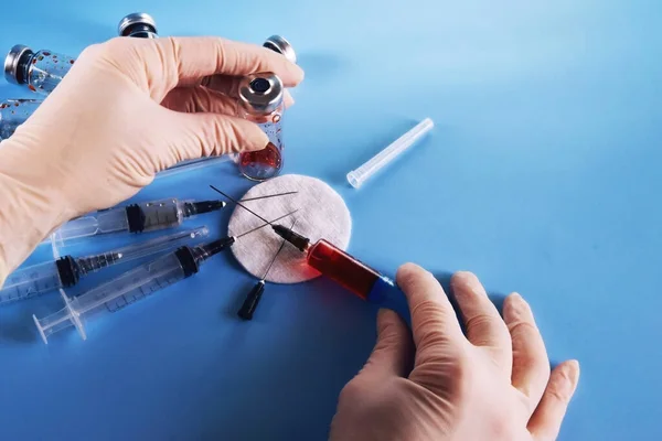 syringe in right hand and glass bottle in left hand against blue defocused background of glass vials and used syringes, beam of light on the right