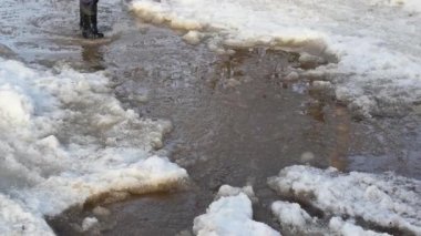 Siyah lastik çizmeli bir çocuk kar birikintisinde yürüyor ve etrafta uçuşan sıçramalar yaratıyor..