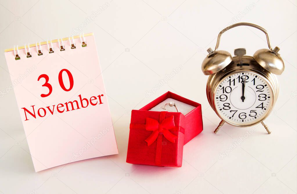 calendar date on light background with red gift box with ring and alarm clock with copy space. November 30 is the thirtieth day of the month.