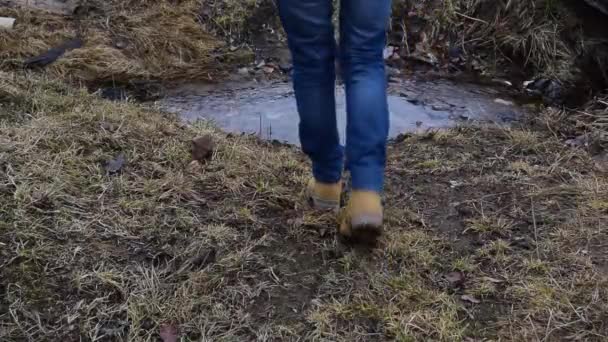 遅い動きで急な地形をハイキングする女性の足の閉じるまで 川を渡って春の道を歩くハイキングブーツの足 — ストック動画