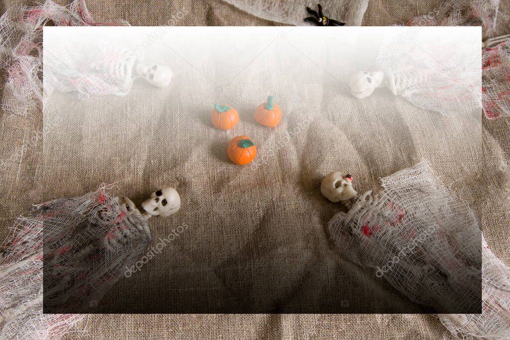 Halloween concept with pumpkins, skeletons and spiders toys on a crumpled gray background with copy space