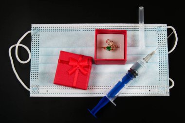Tıbbi maskenin üzerinde bir hediye kutusunda yüzük ve enjeksiyonlu bir şırınga. Coronavirus konseptinde düğün yakın çekim.
