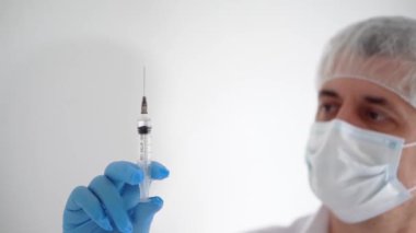 Tıbbi maskeli ve eldivenli bir doktor elinde şırıngayla yakın çekim yapıyor.