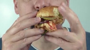 Bir adam açgözlülükle vejetaryen burger yer. Aç orta yaşlı bir adam hamburger yiyor.