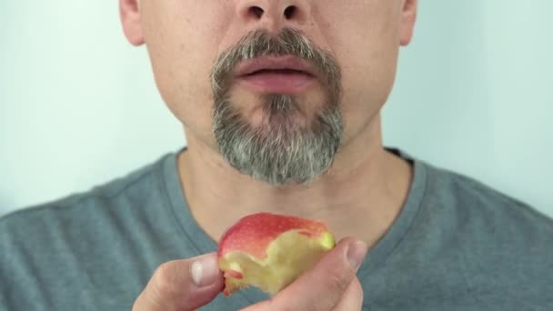 Close-up, um homem com barba e bigode comendo uma maçã vermelha, close-up, 4K — Vídeo de Stock