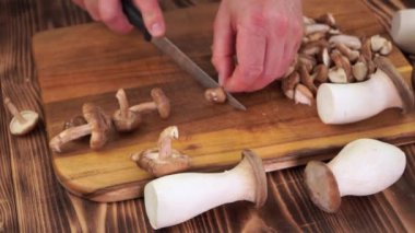 Male hands cut pieces of king oyster mushrooms on wooden boards, slow motion