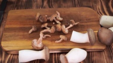 Whole raw shiitake and oyster mushrooms fall on cutting wooden board slow motion