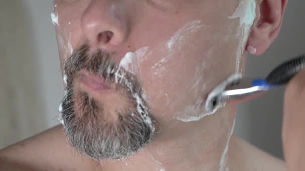 Hombre de mediana edad con espuma en la barba de afeitar la cara con una navaja de afeitar, cerca de 4K — Vídeos de Stock