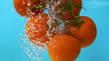 Su kabarcıklarında yüzen domatesler, mavi arkaplan, yavaş çekimde kapat