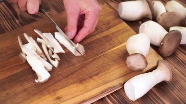 Erkek eller kral istiridye mantarı hazırlıyor. Dilimler, tahta tahta üst görünümü kesiyor.