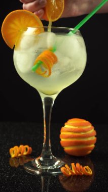 Kadın eli portakalı cin kokteyline sıkıştırıyor, 4k dikey video, kapat.