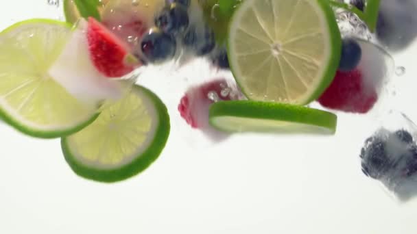 Salpicadura de cubitos de hielo de frutas flotando en agua lima fresa arándano menta de cerca — Vídeo de stock