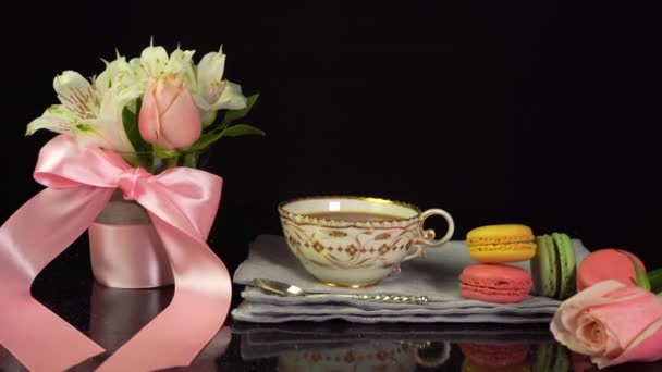 Sammansättning av kopp te, makaroner, bukett blommor, firande bakgrund — Stockvideo