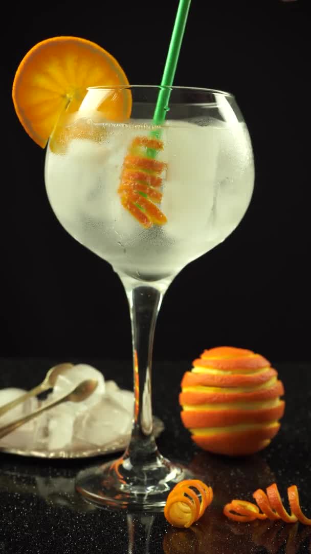 A hand mixing with straw orange peel in gin cocktail, 4k vertical video close up — Stock Video