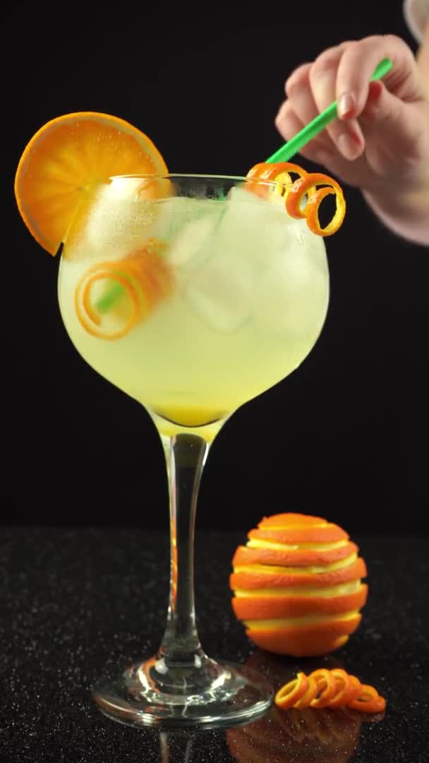Τζιν πορτοκαλί κοκτέιλ με πάγο σε ποτήρι, γυναικείο καλαμάκι κάθετο βίντεο από κοντά — Αρχείο Βίντεο