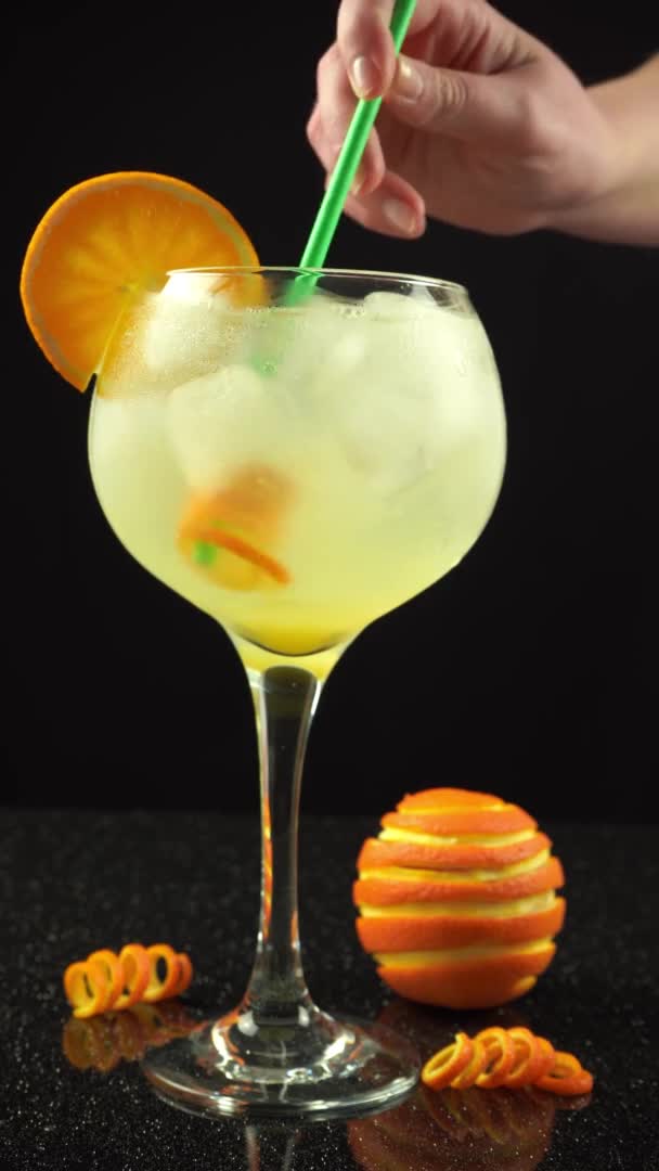 Female hand mixing gin orange cocktail with straw, 4k vertical video, close up — Αρχείο Βίντεο