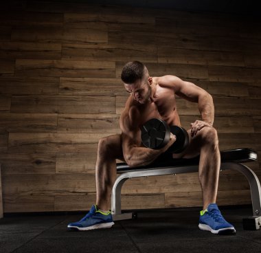 Yakışıklı ve kaslı bir adam, spor salonunda kameraya poz veriyor.