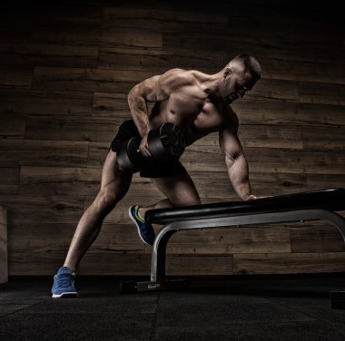 Yakışıklı ve kaslı bir adam, spor salonunda kameraya poz veriyor.