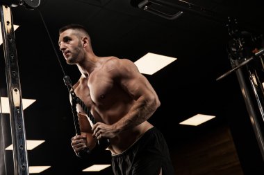 Yakışıklı ve kaslı bir adam, spor salonunda kameraya poz veriyor.