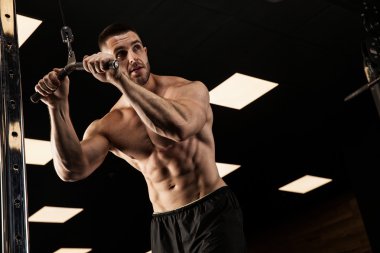 Yakışıklı ve kaslı bir adam, spor salonunda kameraya poz veriyor.