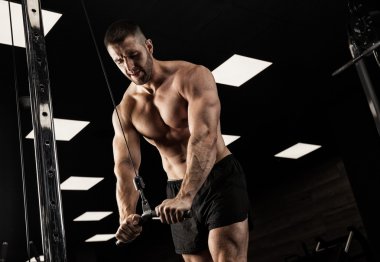 Yakışıklı ve kaslı bir adam, spor salonunda kameraya poz veriyor.