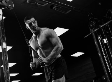 Yakışıklı ve kaslı bir adam, spor salonunda kameraya poz veriyor.