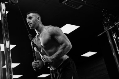 Yakışıklı ve kaslı bir adam, spor salonunda kameraya poz veriyor.