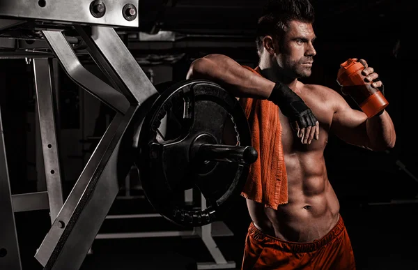 El chico deportivo muy musculoso bebiendo proteína en roo de peso oscuro — Foto de Stock