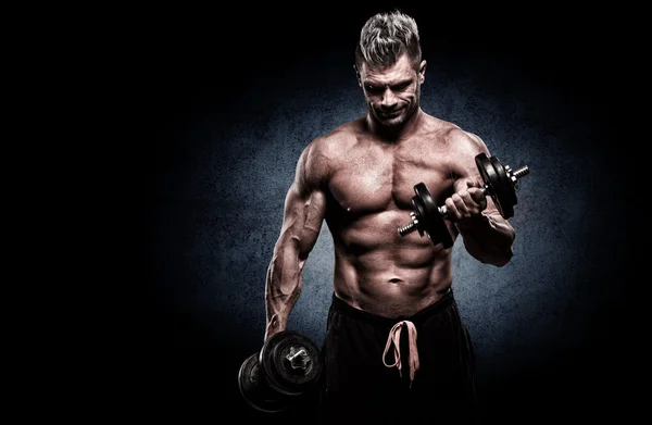 Closeup of a muscular young man lifting weights on dark backgrou — Stock Photo, Image