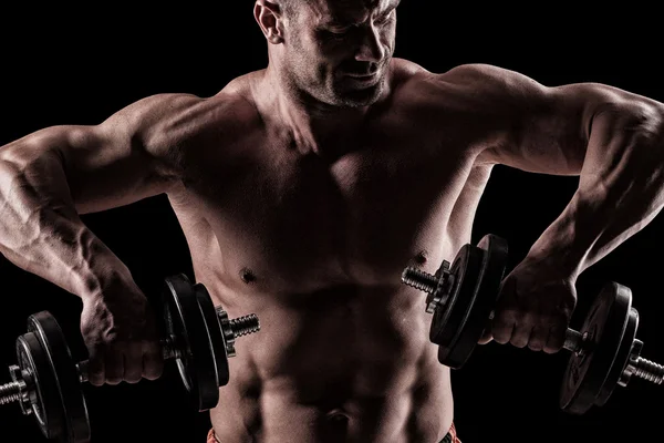 Closeup of a muscular young man lifting weights on dark backgrou — Stock Photo, Image