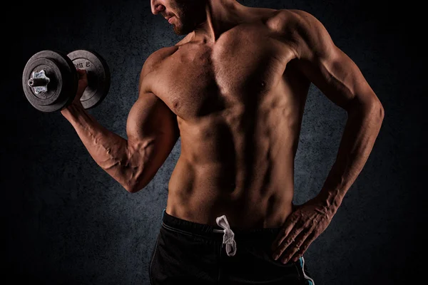 Handsome muscular man working out with dumbbells over black back — Stockfoto