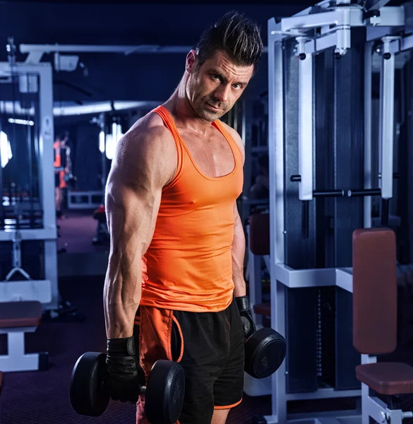 Musculoso hombre haciendo ejercicio con mancuernas mirando a su bíceps bl —  Fotos de Stock