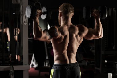 güçlü ve yakışıklı bir genç adam dumbbells ile egzersiz yaparak