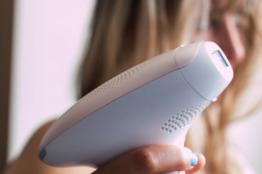 Foto-epilasyon için bir cihaz tutan genç sarışın kadın