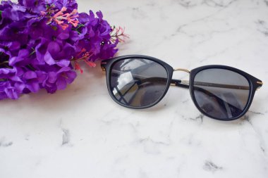 Masada suni çiçeklerin yanında siyah güneş gözlükleri var.