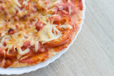 Bir dilim pizza beyaz bir tabakta yatıyor ve masanın üzerinde duruyor, boş bir alan var..