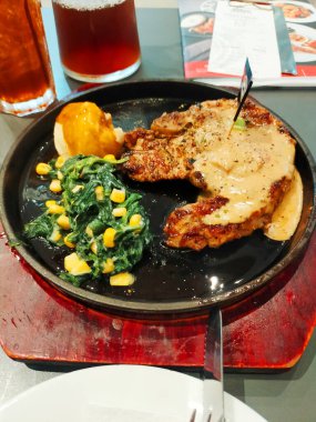 Ahşap masada sıcak tepside sebzeli ızgara domuz pirzolası.