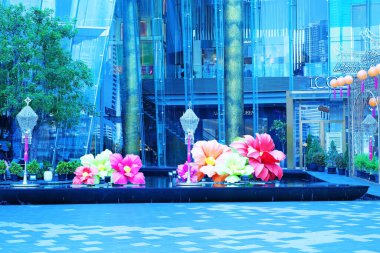 Cam bir binanın önündeki gölün üzerinde renkli çiçekler.