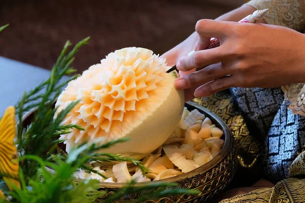Genç bayan el işi, açık sarı bir kavunu bulanık arka planda güzel bir çiçeğe çeviriyor.