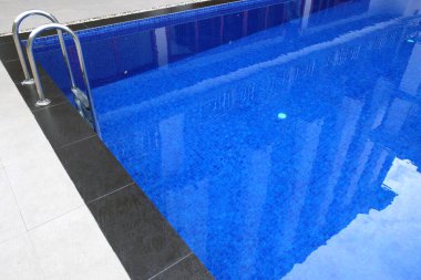 Güneşli yansımalı mavi yüzme havuzuna merdiven dayayın.