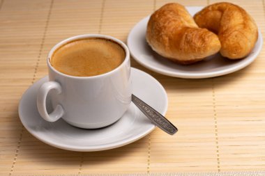 Sabah aromatik kahve ve iki taze kruvasan doğal bambu seçici odak noktasından yapılmış bir peçetede beyaz bir tabakta.