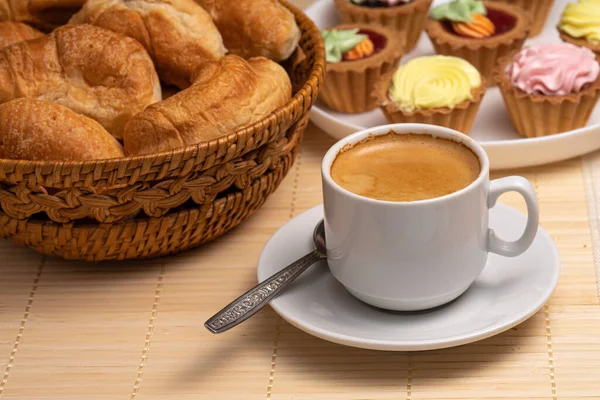 Café con croissants frescos en una cesta de mimbre y pasteles en un plato blanco en una servilleta hecha de bambú natural —  Fotos de Stock