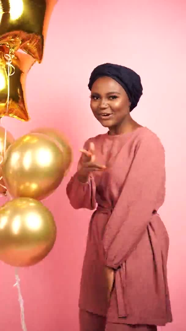 Schwarze Mädchen mit goldenen Luftballons feiern und lächeln isoliert auf Pfirsichhintergrund. Afrikanische Frauen feiern ihren Abschluss. Glückliches Gefühl einer muslimischen jungen Frau — Stockvideo
