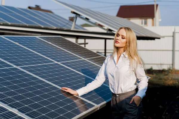 Woman leans on solar panels. Blonde dressed white formal shirt on the power plant. Free electricity for home. Green energy. Solar cells power plant business.